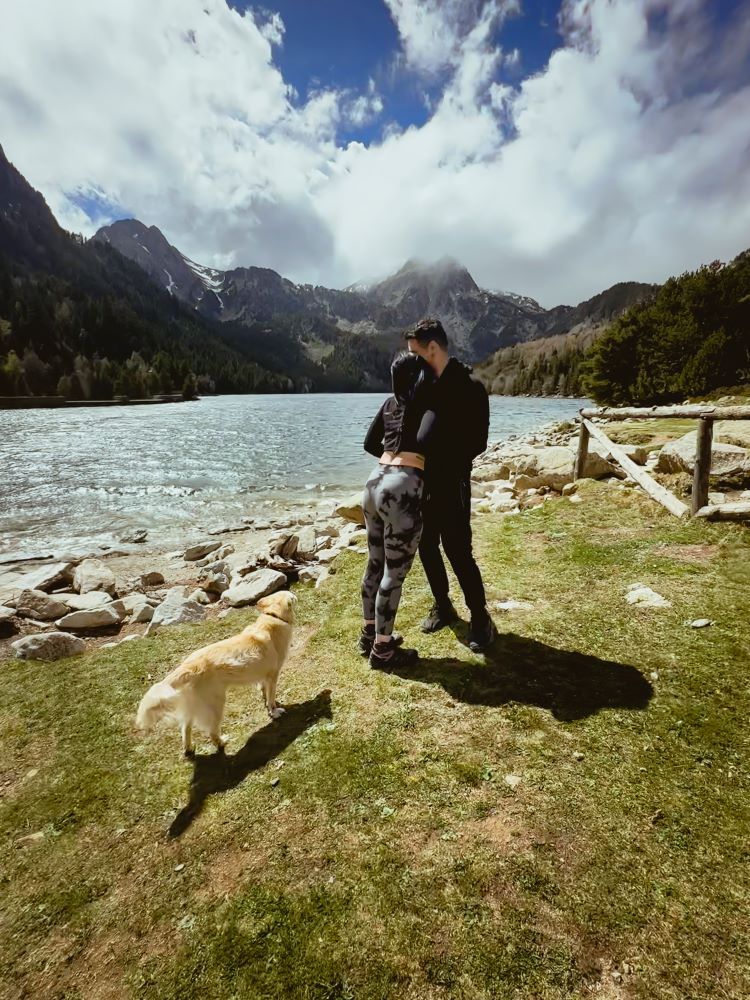 pareja mirando el lago de espaldas a la camara vestido de negro y perro pequeño rubio en el lado izquierdo en lleida